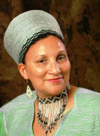 Gertrude Fester posing with brown background wearing green top with matching green hat and beaded necklace