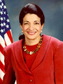 Senator Olympia Snowe wearing red suit with American flag behind her